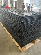 Stack of black metal grating on a wooden pallet with people in the background.