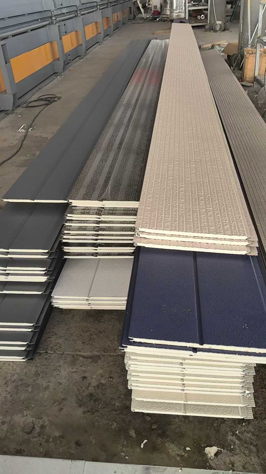 Stacks of metal roofing panels on a concrete floor with a building in the background.