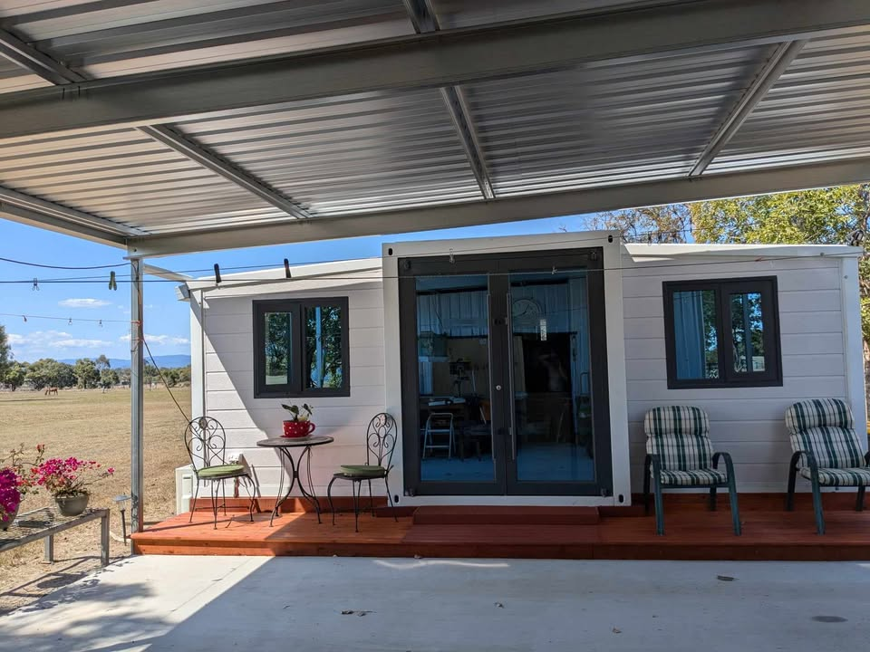 Expandable white house with a patio area featuring chairs and a table.