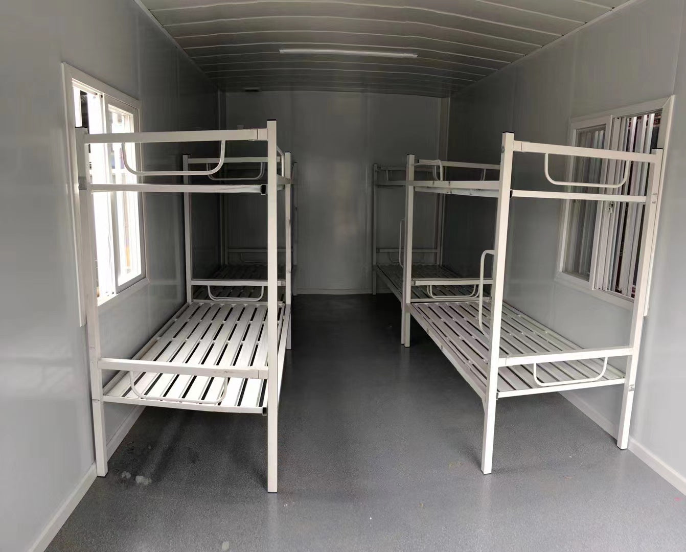 Two white metal bunk beds in a small room with gray walls and floor.
