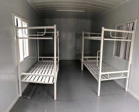Two white metal bunk beds in a small room with gray walls and floor.