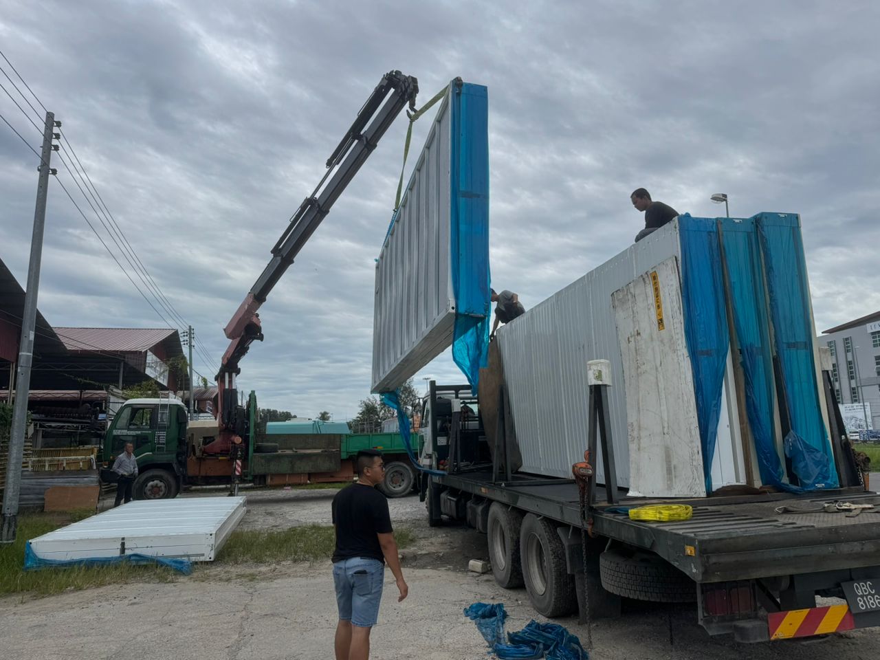 Loading of large white panels onto a truck with a crane under a cloudy sky.