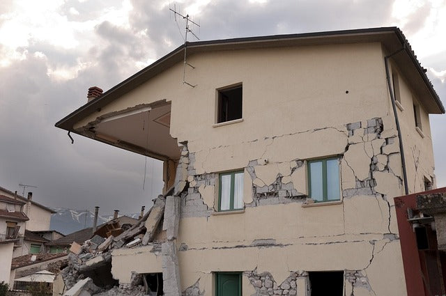 Damaged house with cracks and missing parts under a cloudy sky